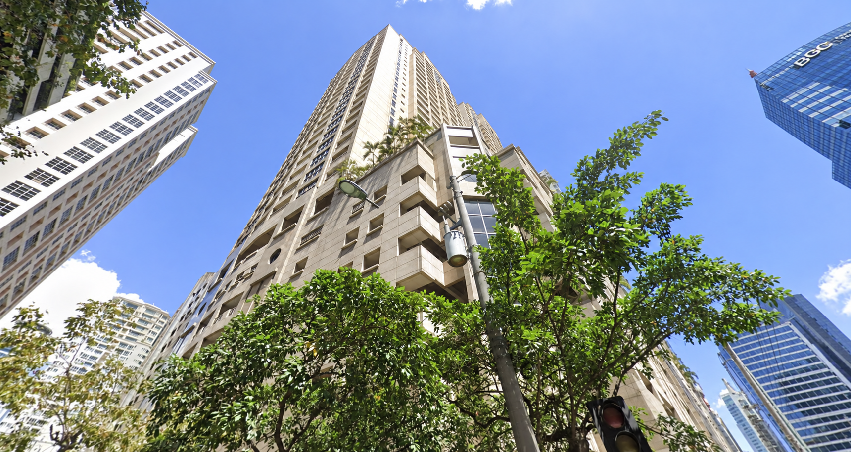 High-rise building viewed from street level with greenery and blue sky in Makati City